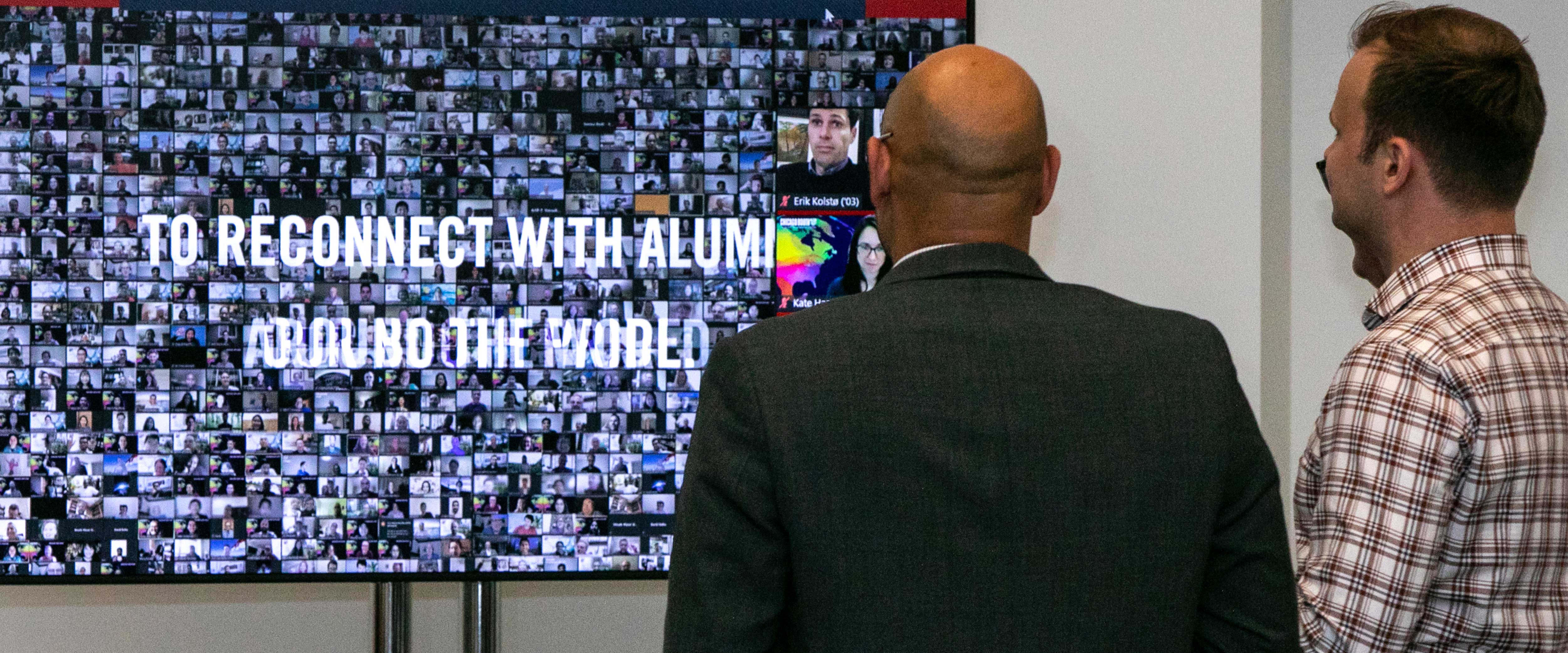 Two men watching Chicago Booth alumni zoom squares on a large monitor