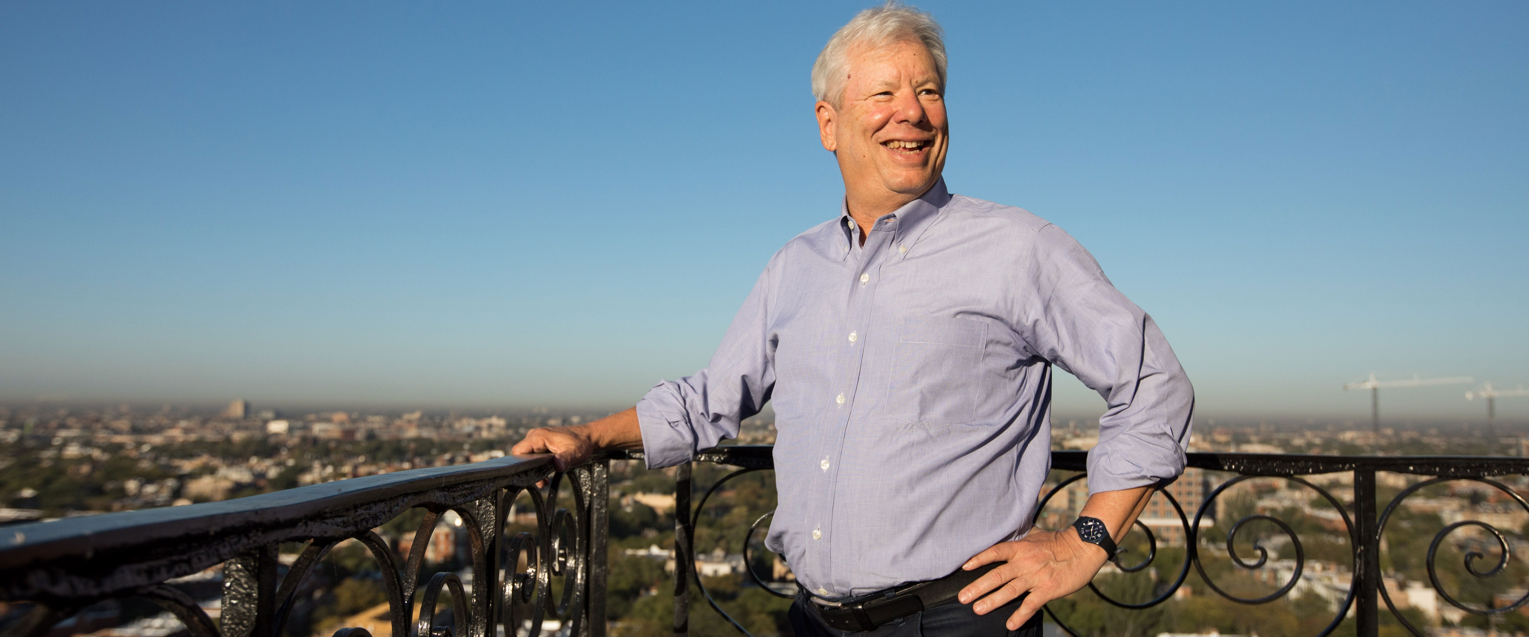 Richard Thaler smiles on his balcony overlooking green trees