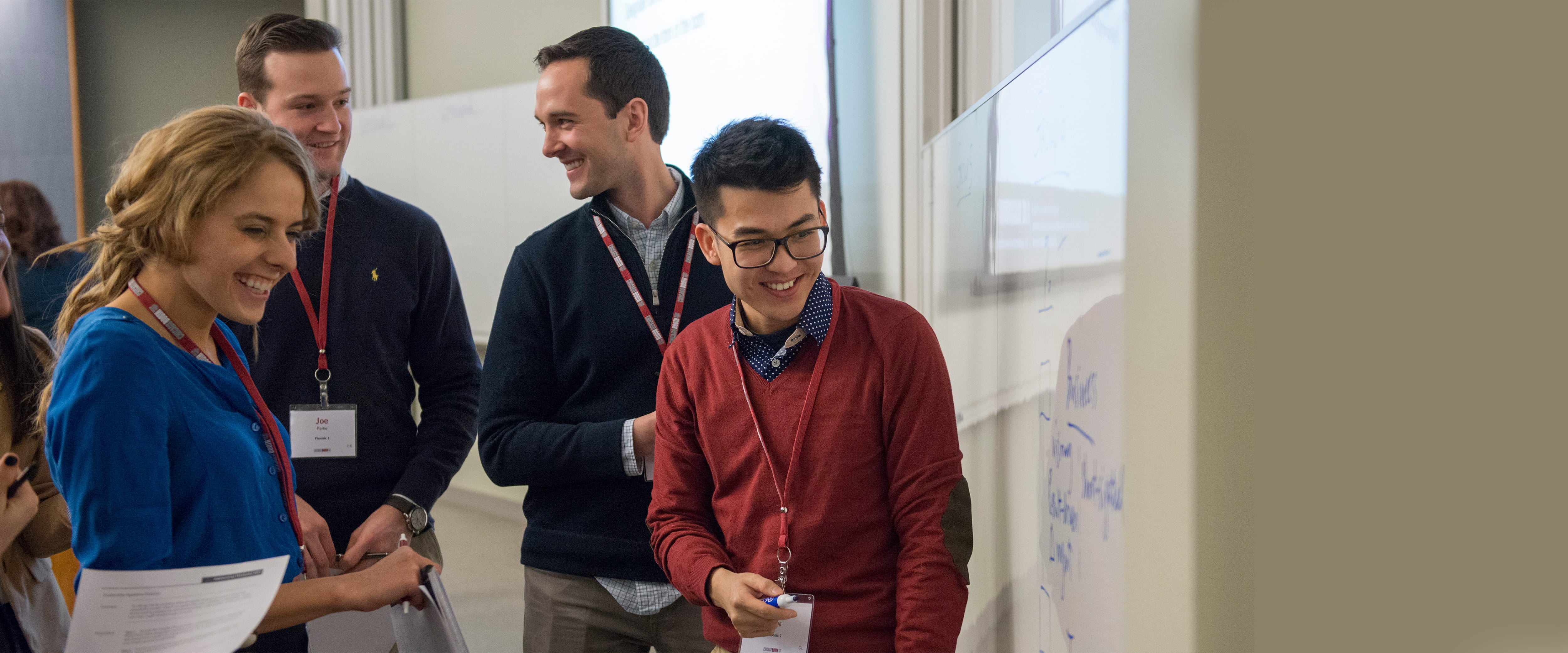 Group of male and female students gathered around a white board, working together
