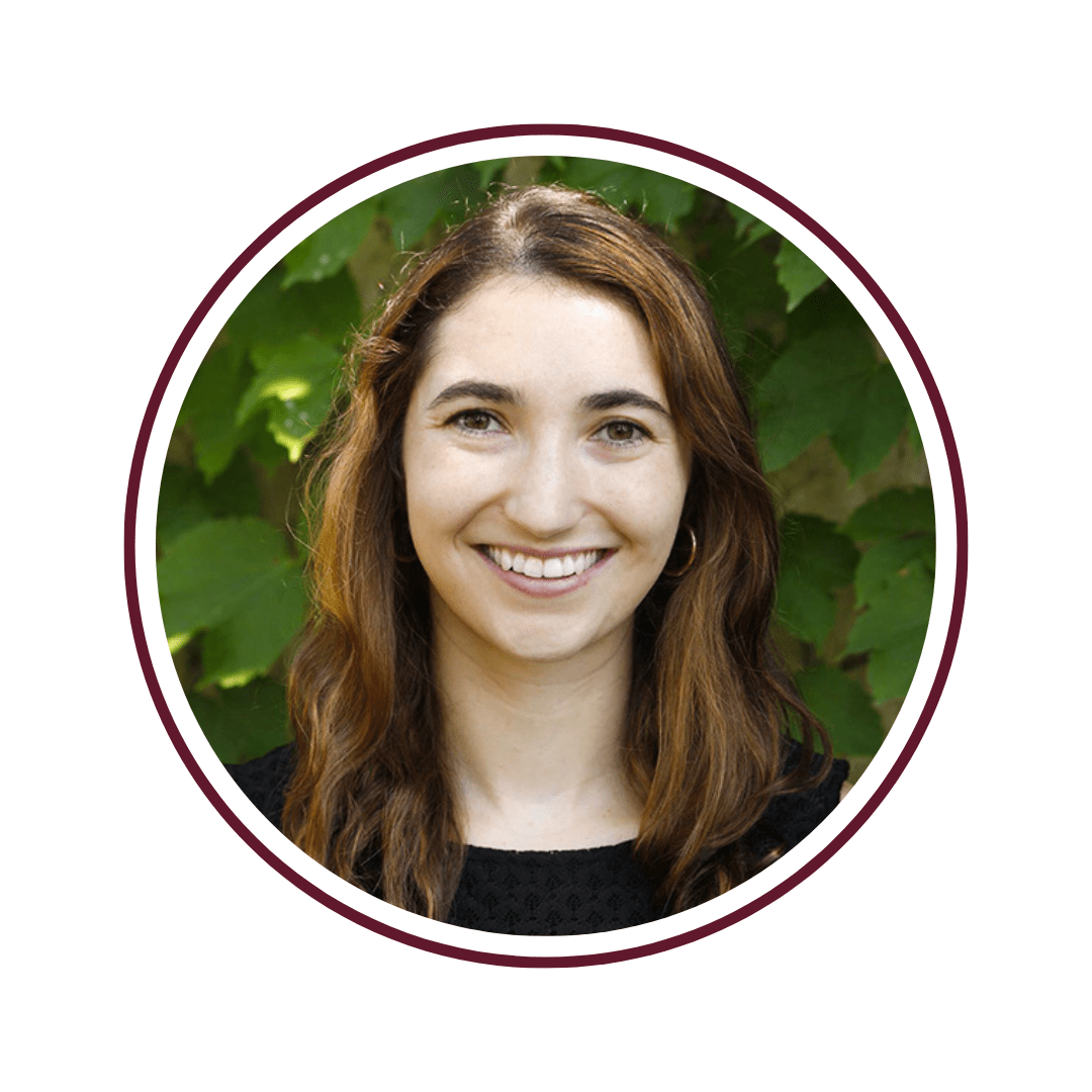 Young auburn-haired woman smiling in front of a green-vine background. 