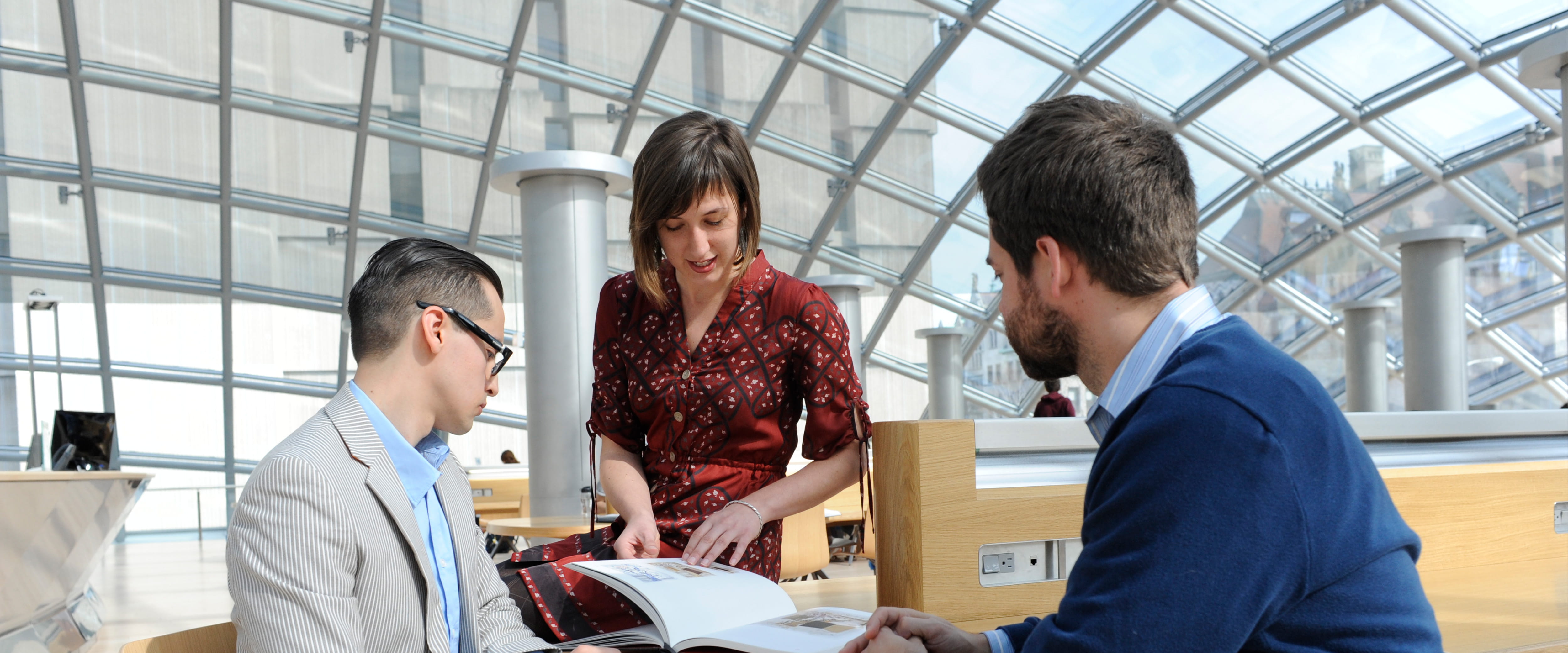 Three students gather around a book at a desk in the Regenstein Library.