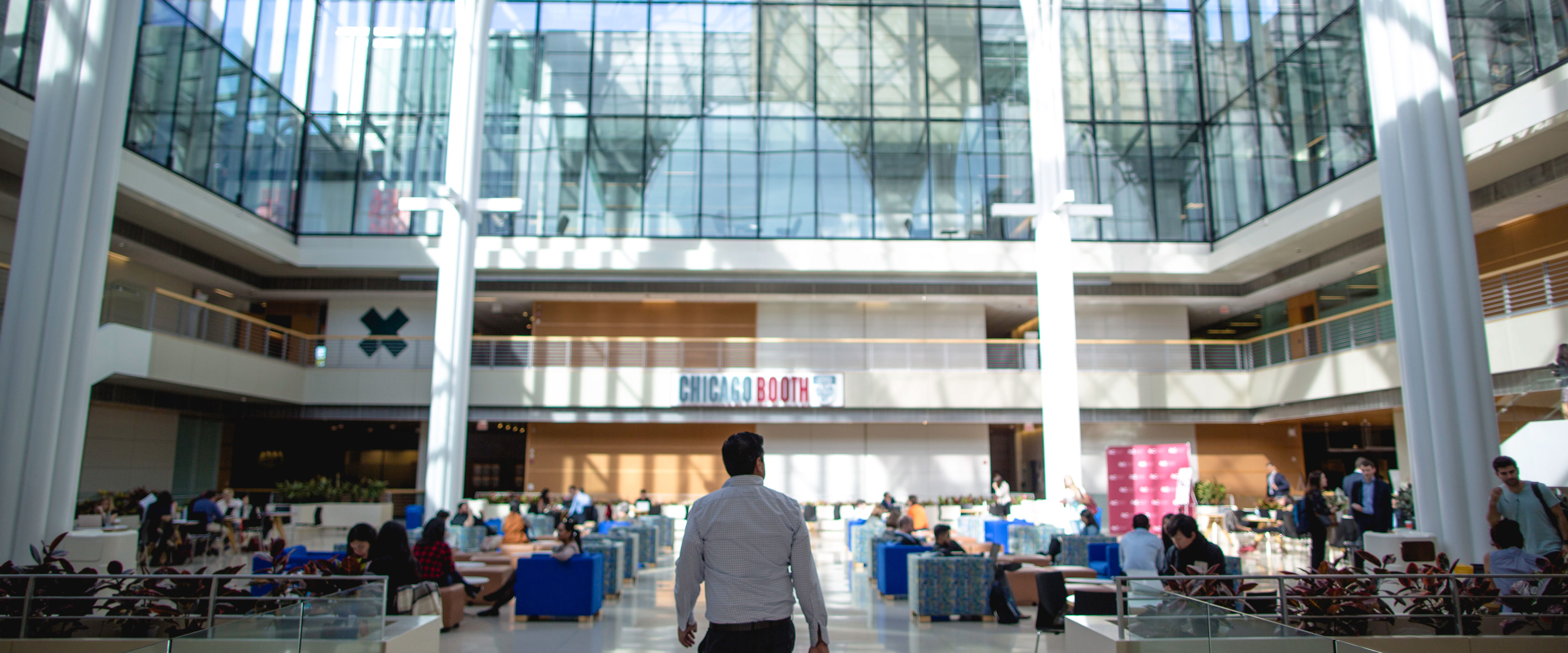A man walks into the center of the Harper Center Winter Garden, looking up at the grand windows. 