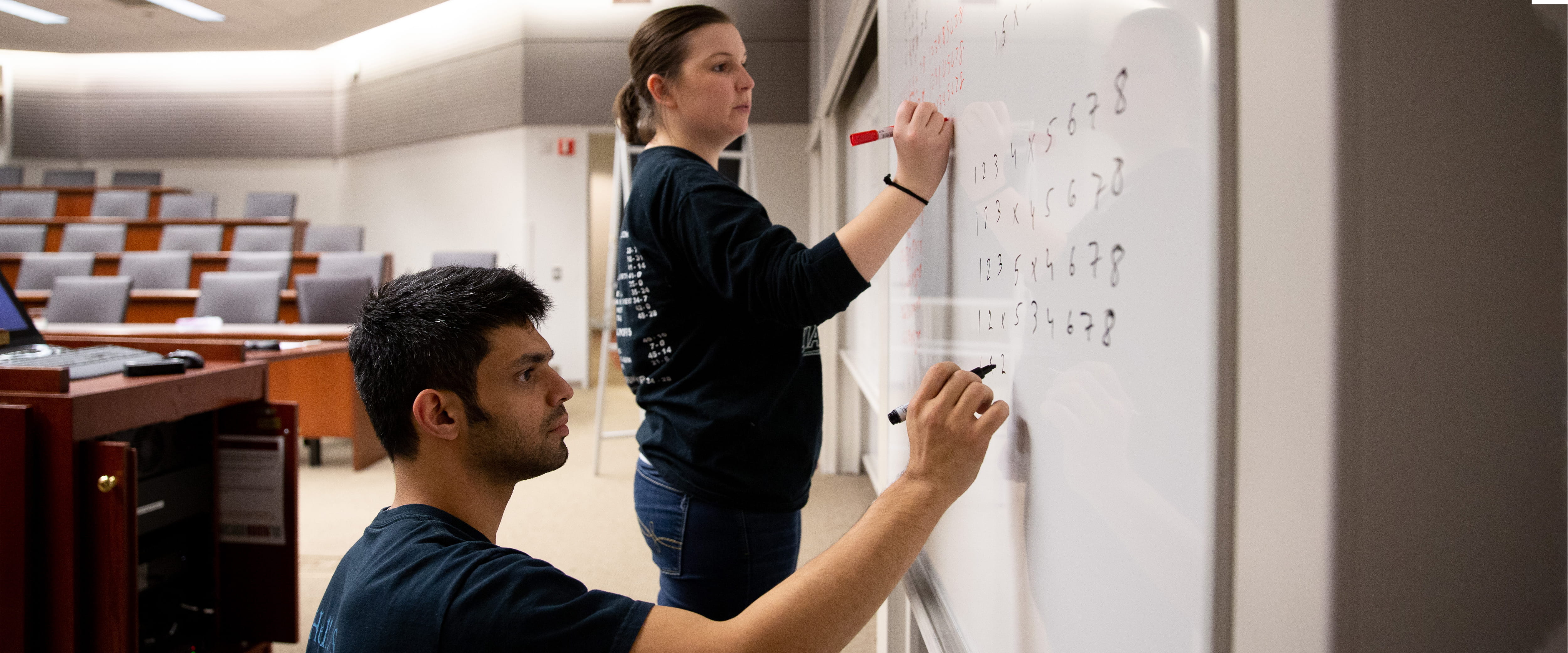 A man and woman writing on the whiteboard