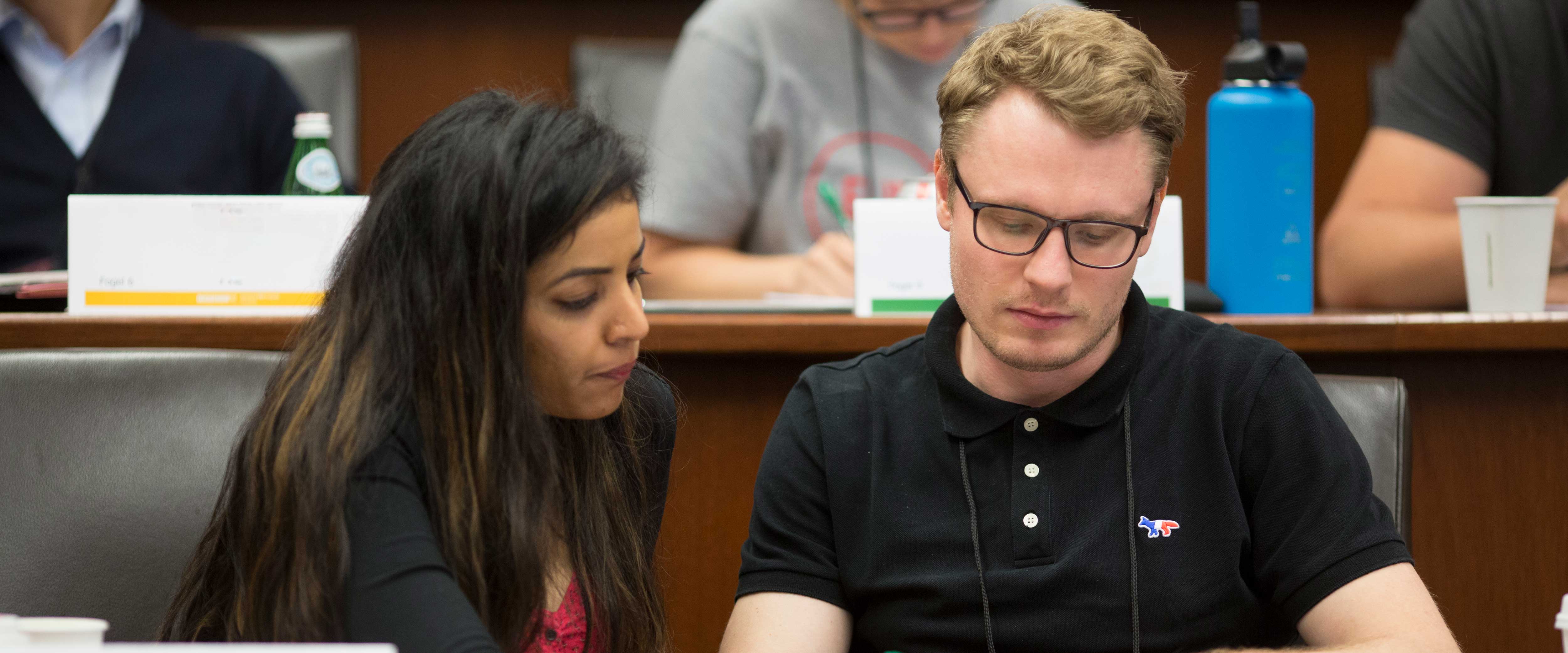 Two students seated next to eachother in a tiered classroom working on a project together